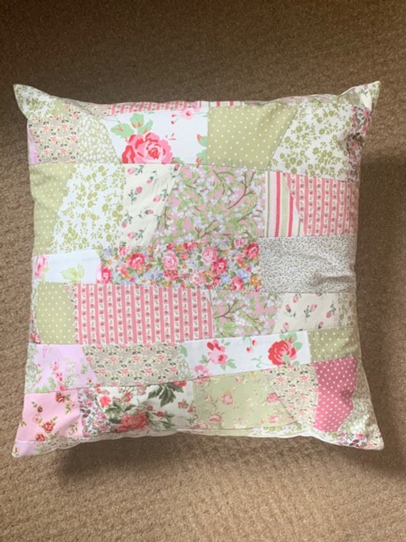 May include: A patchwork pillow with a floral design in shades of pink, green, and white. The pillow is made of different fabrics and has a quilted look.