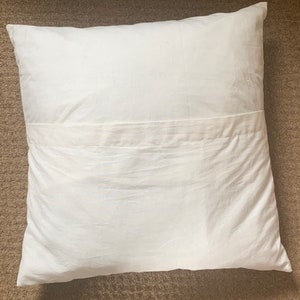 May include: A white pillow with a seam down the middle. The pillow is made of a soft, smooth fabric.