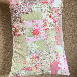 May include: A patchwork pillow with a floral design in shades of pink, green, and white. The pillow is made of different fabrics and has a quilted texture.