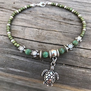 May include: Green beaded ankle bracelet with a silver turtle charm. The bracelet has small silver turtle beads and a silver bead with a textured surface.