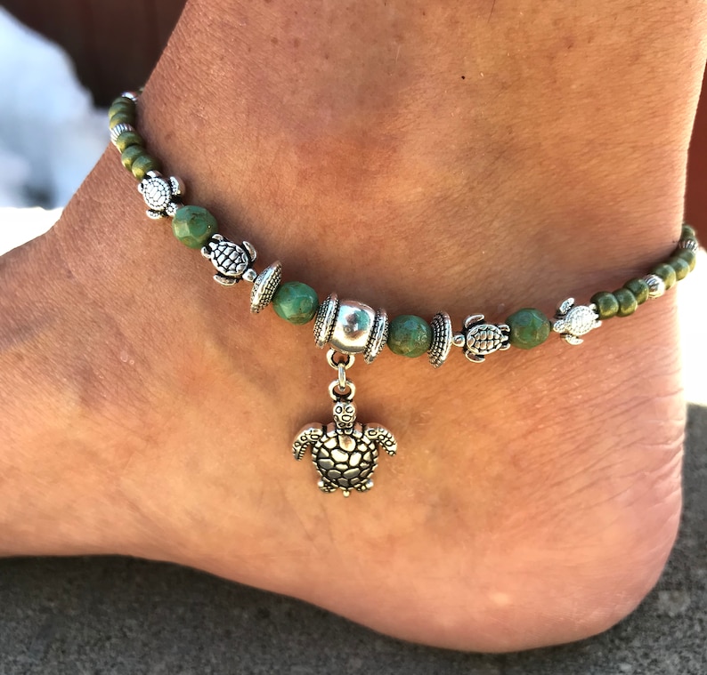 May include: Green and silver anklet with a charm of a turtle. The anklet is made of small green beads and silver turtle charms.