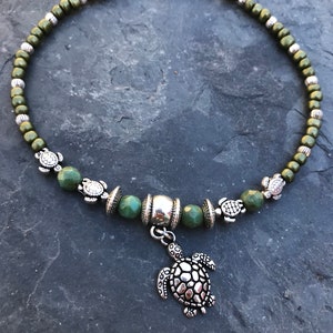 May include: A green beaded anklet with a silver turtle charm. The anklet has a silver clasp and is decorated with small silver turtle beads.
