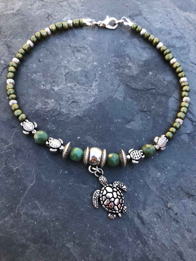 May include: A green beaded anklet with a silver turtle charm. The anklet has a silver clasp and is decorated with small silver turtle beads.