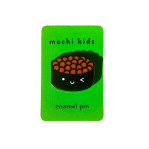 Puede incluir: Tarjeta verde con el texto "mochi kids" y "enamel pin" en negro. Un pin de esmalte negro y marrón de un rollo de sushi con una cara linda.