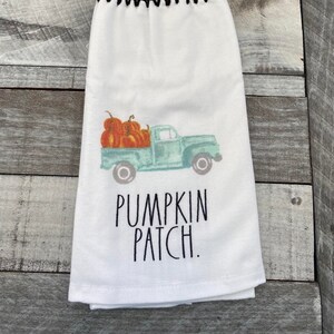 May include: White kitchen towel with a black crocheted hanging loop and a button. The towel features a vintage truck carrying pumpkins and the text "Pumpkin Patch."