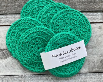 Peut inclure: Un ensemble de six éponges à récurer le visage en crochet vert. Les éponges sont faites de fil de coton 100% et sont lavables en machine. Le texte "Face Scrubbies 100% Cotton Yarn Machine Washable" est imprimé sur une étiquette blanche.