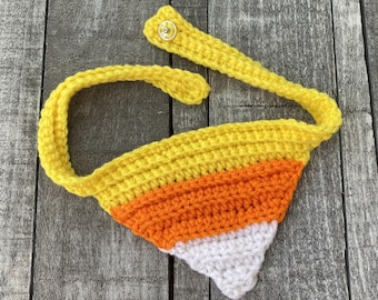 May include: A crocheted candy corn-shaped dog bandana with yellow, orange and white stripes. The bandana has a yellow strap with a snap closure.