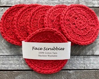 Peut inclure: Six éponges à récurer le visage en crochet rouge, en fil de coton 100 %. Les éponges sont lavables en machine. Le texte "Face Scrubbies 100% Cotton Yarn Machine Washable" est imprimé sur une étiquette blanche.