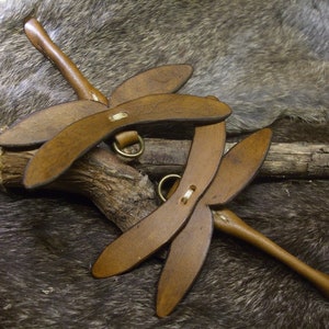 May include: Two brown leather dragonfly-shaped keychains with brass accents. The keychains are lying on a brown furry surface.