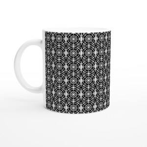 May include: White ceramic mug featuring a repeating pattern of white ornate circular designs on a black background. The mug has a white handle and a glossy finish. The design is symmetrical and detailed, creating a visually appealing contrast.