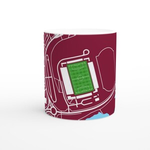May include: White ceramic mug with a detailed map illustration of a stadium. The design features a green pitch, white lines, and a maroon background. The mug is cylindrical and has a glossy finish.