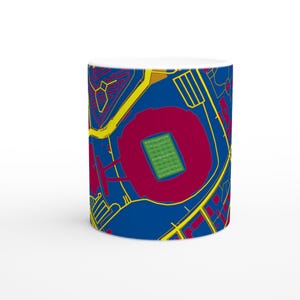 May include: White ceramic mug featuring a stadium map design. The map is in blue, yellow, red, and green, with a detailed illustration of the stadium and surrounding areas. The mug is a standard size.