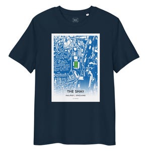 Puede incluir: Camiseta azul marino con un diseño gráfico rectangular blanco. El gráfico muestra un mapa detallado en azul y blanco de una ciudad, con un rectángulo verde que representa un campo deportivo. El texto en la parte inferior dice "THE SHAY HALIFAX | ENGLAND".