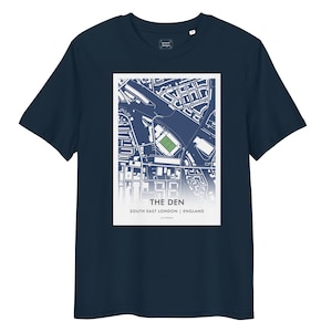 May include: Navy blue t-shirt featuring a white rectangular graphic. The graphic displays a map of an area with a green stadium and the text "THE DEN SOUTH EAST LONDON | ENGLAND". The shirt is made of a soft material.