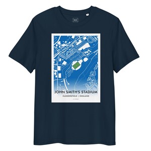 May include: Navy blue t-shirt featuring a white and blue graphic of John Smith's Stadium in Huddersfield, England. The graphic includes the stadium's layout and surrounding streets. The text "JOHN SMITH'S STADIUM" is printed below the map.