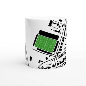 Puede incluir: Taza de cerámica blanca con un diseño de mapa arquitectónico en blanco y negro. El mapa incluye un campo de fútbol verde, edificios y carreteras. La taza es cilíndrica y tiene un acabado brillante.