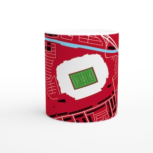 Op de afbeelding: Witte keramische mok met een gedetailleerde kaartillustratie van een stadion. Het ontwerp is voornamelijk rood met witte en zwarte accenten, inclusief de stadionomtrek, wegen en gebouwen. Het veld is groen, een blauwe rivier is zichtbaar.