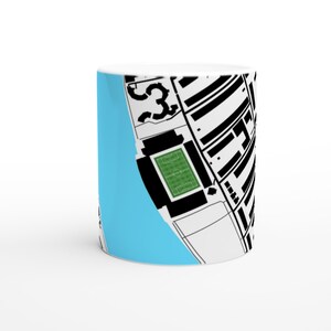 May include: White ceramic mug featuring a black and white architectural design with a light blue background. The design includes a soccer field and the number 53.
