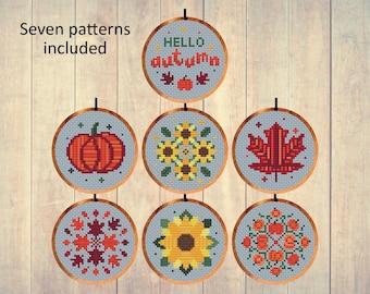 May include: Cross-stitch patterns featuring autumn themes. Designs include a pumpkin, sunflowers, and a maple leaf, all within circular frames. The text "HELLO autumn" is also included. Seven patterns are included.