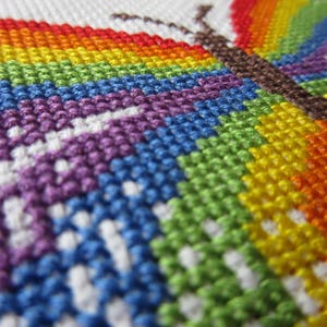 May include: Close-up of a colorful cross-stitch embroidery of a butterfly with a rainbow wing pattern.
