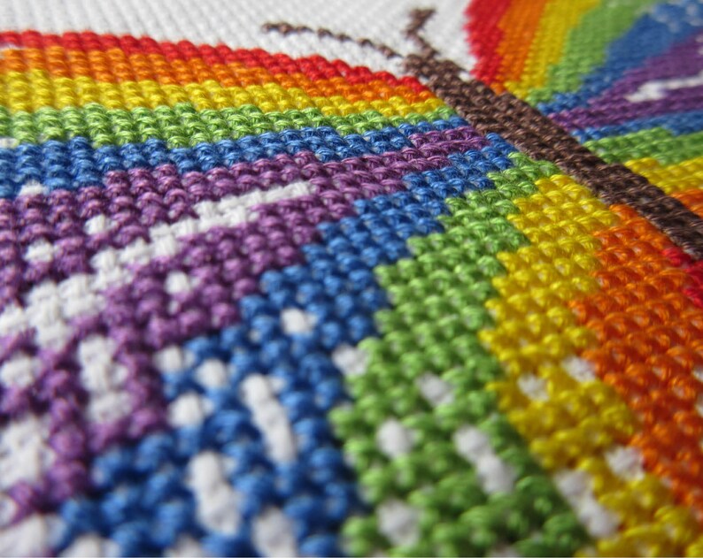 May include: Close-up of a colorful cross-stitch embroidery of a butterfly with a rainbow wing pattern.