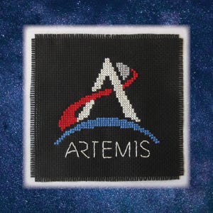 May include: A black square patch with the word "ARTEMIS" embroidered in white. The patch features a stylized "A" with red, white, and blue accents. The background is a starry night sky.