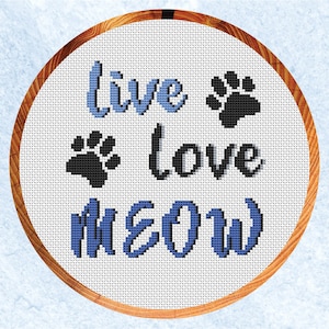 May include: A white embroidery hoop with a blue and black cross-stitch design that reads "Live Love Meow" with paw prints.