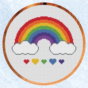 Pode incluir: Um padrão de ponto cruz com um arco-íris, nuvens e corações. O arco-íris é feito de vermelho, laranja, amarelo, verde, azul, anil e violeta. As nuvens são brancas e os corações são vermelhos, amarelos, verdes, azuis e roxos.