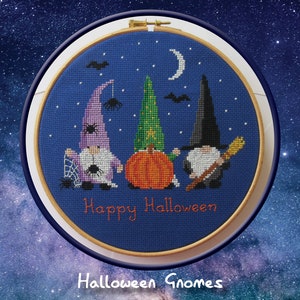 May include: A blue and white cross-stitch embroidery hoop with a Halloween theme. The design features three gnomes, a pumpkin, a spider web, and the text "Happy Halloween".