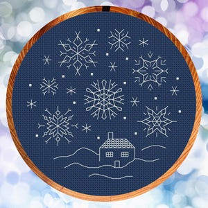 May include: A blue embroidery hoop with a white outline of a house and snowflakes on a dark blue background.
