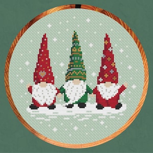 May include: Three gnomes wearing red and green hats stand in a snowy scene. The gnome in the middle is wearing a green hat with a white trim and a green beard. The gnomes on either side are wearing red hats with white trim and red beards.