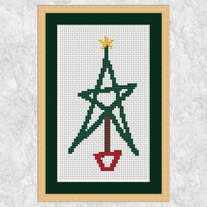 May include: A framed cross-stitch of a Christmas tree. The tree is green with a gold star on top, a brown trunk, and a red pot. The artwork is framed in a gold-colored frame with a green mat.