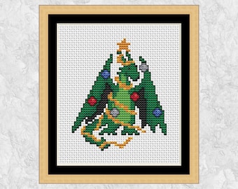 May include: Cross-stitch art of a green dragon decorated as a Christmas tree, with ornaments and a star on top. The dragon is framed in a wooden frame with a black border, set against a white background.