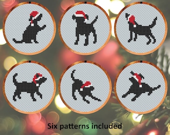 May include: Six different cross-stitch patterns featuring black dogs wearing Santa hats. The patterns are displayed in white embroidery hoops on a blurry background of Christmas lights.