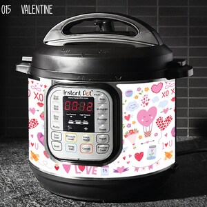 May include: A white Instant Pot with a Valentine's Day themed design. The design features hearts, flowers, and the words "XO" and "I love you".