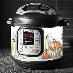 May include: A white Instant Pot with a digital display and a pumpkin themed design. The design features a watercolour style with pumpkins in shades of white, orange, and green.