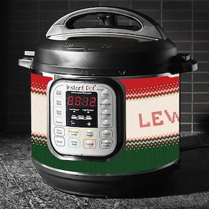 Puede incluir: Una olla a presión eléctrica Instant Pot negra con un diseño de suéter navideño rojo, blanco y verde. La pantalla muestra "88:88" y la palabra "LEW" está impresa en la parte delantera.