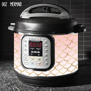 Puede incluir: Una olla a presión Instant Pot rosa y dorada con un diseño de escamas de sirena. La pantalla digital muestra "88:88".