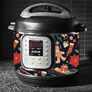 Op de afbeelding: Een zwarte Instant Pot elektrische snelkookpan met een kerstthema. Het ontwerp bevat peperkoekmannetjes, snoepstokken, sneeuwvlokken en kerststerren op een donkerblauwe achtergrond.