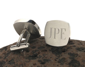 May include: A pair of silver cufflinks with a square shape. One cufflink has the initials "JPE" engraved on it. The other cufflink has "Stainless Steel" engraved on it.