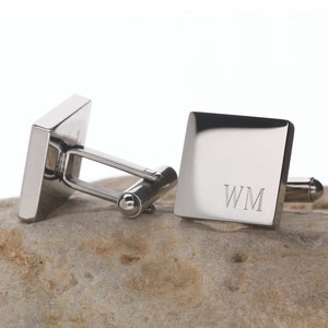 May include: A pair of silver cufflinks with a square shape. The cufflinks are engraved with the initials "WM".