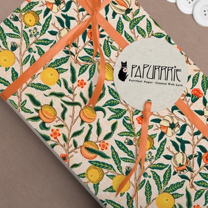 Puede incluir: Un regalo envuelto en papel estampado blanco y naranja con un dise&ntilde;o de melocot&oacute;n y hojas. El papel est&aacute; atado con una cinta de color melocot&oacute;n y una etiqueta redonda con el texto "PAPURRIE Perfect Paper - Created With Love".