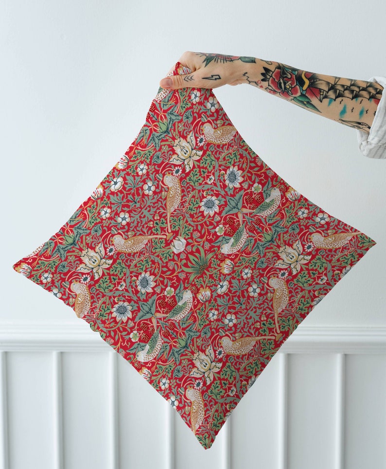 May include: Red fabric with a repeating pattern of stylized birds, flowers, and leaves. The fabric is folded in half and held by a hand.