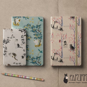 May include: Three different notebooks with cat illustrations. The notebooks have a variety of designs, including bamboo, flowers, and branches. The notebooks are all closed and have a white background. The text "PAPURRIE" is visible in the bottom right corner of the image.