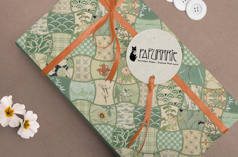 May include: A gift box wrapped in green and beige patterned paper with an orange ribbon. The paper features a variety of Japanese-inspired designs, including waves, flowers, and geometric patterns. A round sticker with the text "PAPURRIE Perfect Paper - Created With Love" is attached to the box.