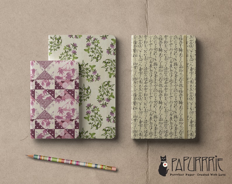 May include: Three different patterned notebooks, one with a floral design, one with a geometric pattern, and one with Japanese characters. The notebooks are on a brown surface with a pencil and a black cat logo with the text "Papurrie Purrfect Paper - Created With Love".