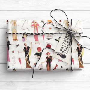 Op de afbeelding: Wit cadeaupapier met een herhalend patroon van vrouwen in vintage kleding, vogels, vlinders en andere decoratieve elementen. Het cadeaupapier is vastgebonden met een zwart-witte touw strik en heeft een label met de tekst "PARCURIA - Perfect papier voor geschenken".