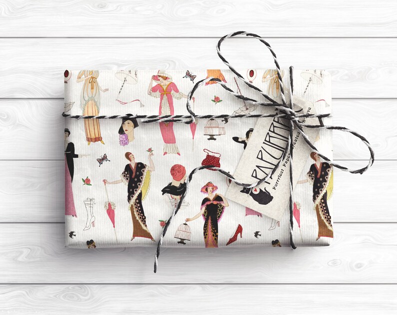Op de afbeelding: Wit cadeaupapier met een herhalend patroon van vrouwen in vintage kleding, vogels, vlinders en andere decoratieve elementen. Het cadeaupapier is vastgebonden met een zwart-witte touw strik en heeft een label met de tekst "PARCURIA - Perfect papier voor geschenken".