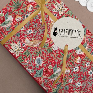 May include: A red and green patterned gift wrap with a gold ribbon and a round tag that says "PAPURRIE Perfect Paper - Created With Love".