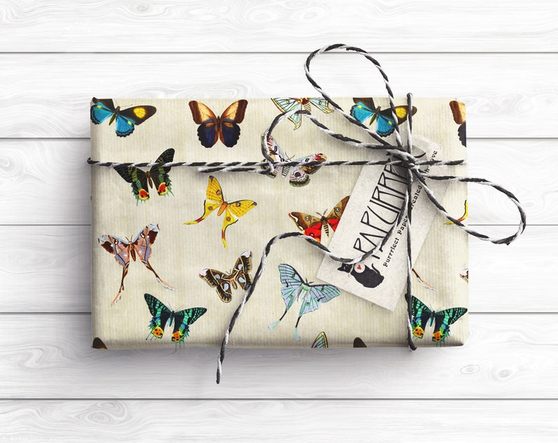 May include: A gift wrapped in brown paper with a black and white string bow. The paper is decorated with a repeating pattern of colorful butterflies. A white tag with black text reads "FANCIFUL Perfect Paper for the Gifted".